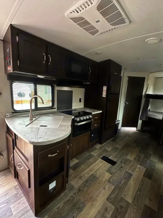 Spacious RV rental kitchen with dark wood cabinets, microwave, stove, and light wood-look flooring. Ready for travel.. Keystone RV Springdale 2021