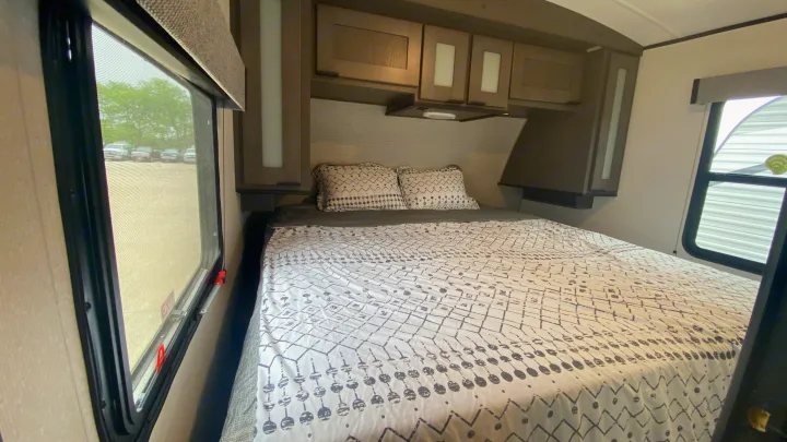 Inside an RV rental, a cozy bedroom with patterned bedding, overhead storage, and large windows offers comfort.. Cruiser Rv Corp Cruiser 2021