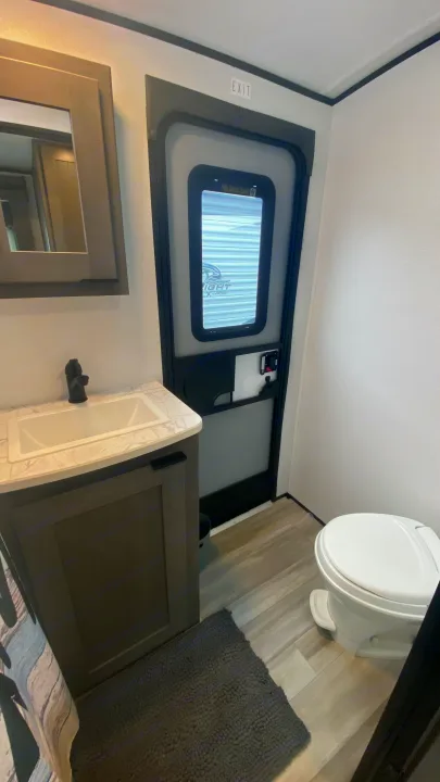 RV rental's compact bathroom features: sink, mirror, vanity, toilet, and main RV entry door with "EXIT" sign visible.. Cruiser Rv Corp Cruiser 2021
