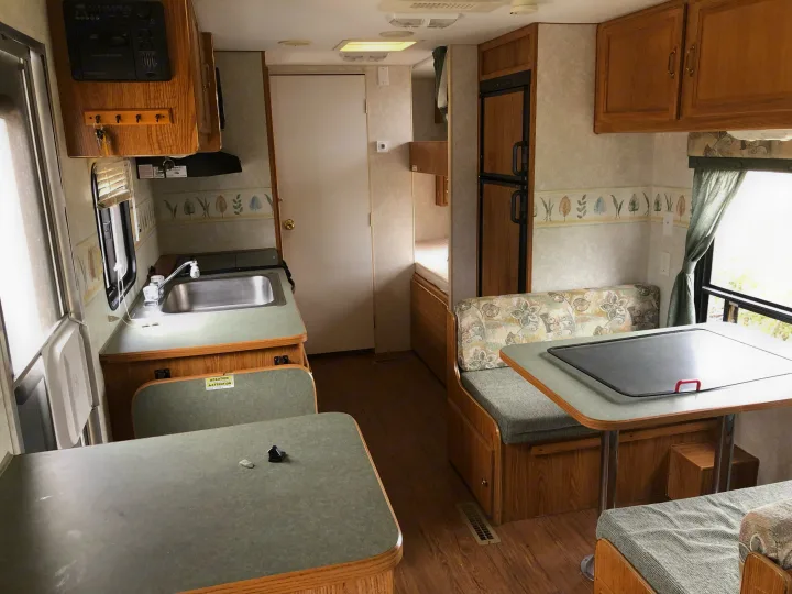 RV rental interior with kitchen, dinette, and sleeping area. Features wood cabinetry, light walls, and green counters.. Wilderness Lite 2003