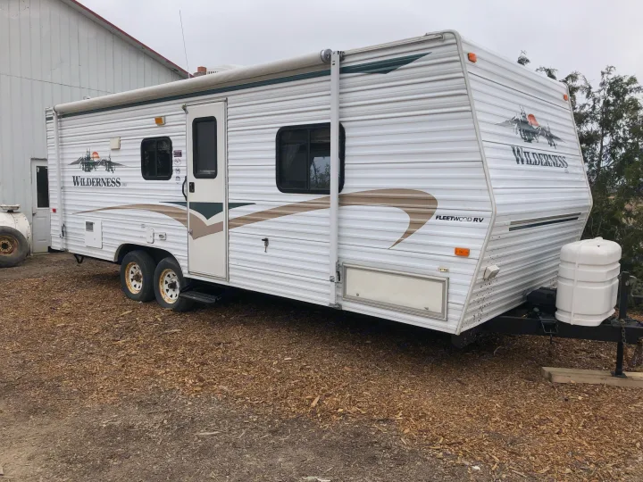White Fleetwood Wilderness travel trailer, ideal for an RV rental, parked outside.. Wilderness Lite 2003