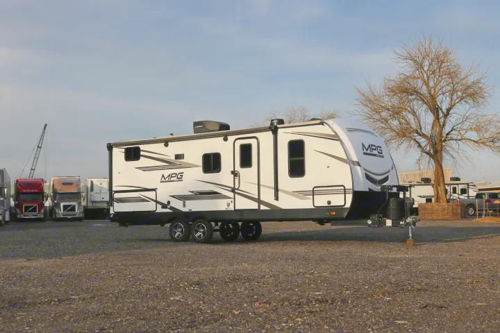 White MPG Ultra-Lite travel trailer, ideal for rv rental, parked on a gravel lot with trucks and a tree.. Cruiser RV MPG Ultra Lite 2022