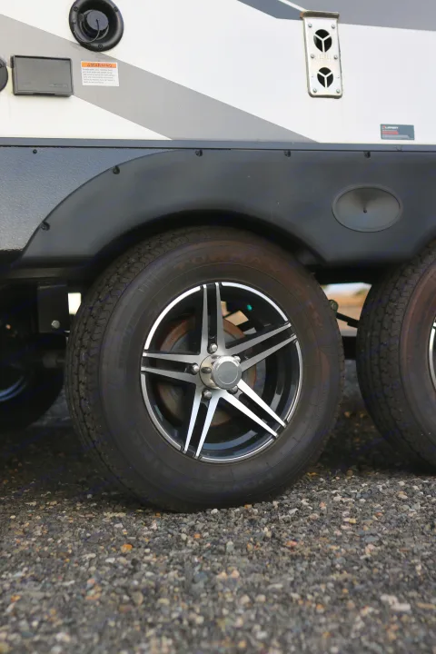 Close-up of an RV rental's wheels, tires (ST205/75R15), side panel with utility hookups & warning label on gravel.. Cruiser RV MPG Ultra Lite 2022