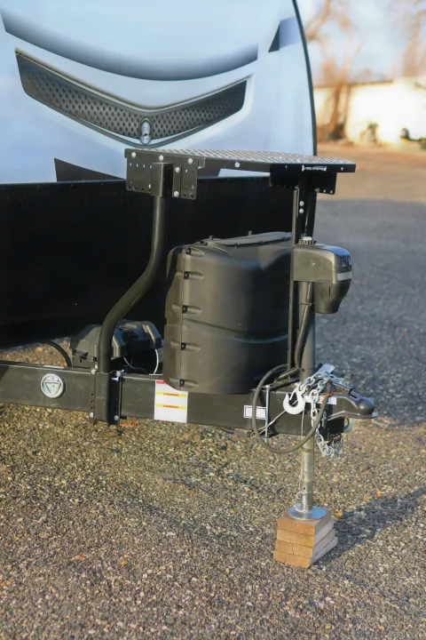 Front of an RV rental trailer showing the electric jack, propane tank cover, hitch, and safety chains on gravel.. Cruiser RV MPG Ultra Lite 2022