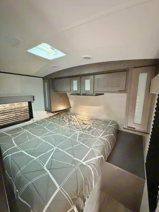 Inside an RV rental, this cozy bedroom features a bed with grey patterned comforter, overhead storage, and a skylight.. Cruiser RV MPG Ultra Lite 2022
