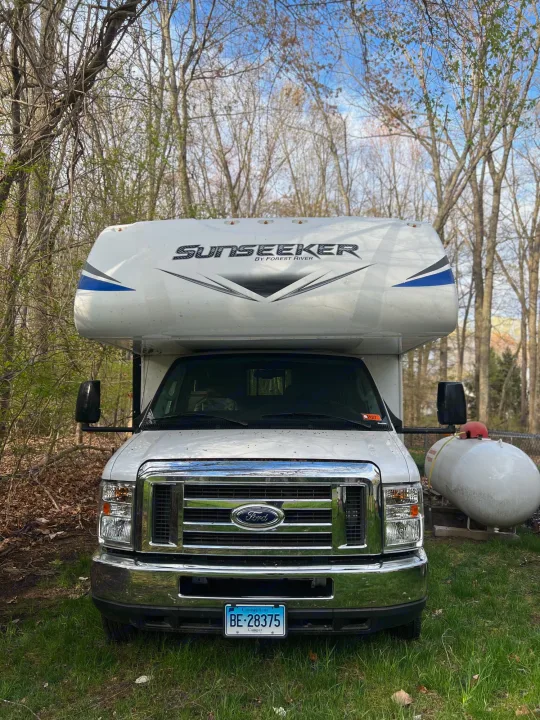 White Sunseeker rv rental camper parked in a wooded setting. Front view showing Ford grill & CT plate.. Forest River Sunseeker Classic 2020