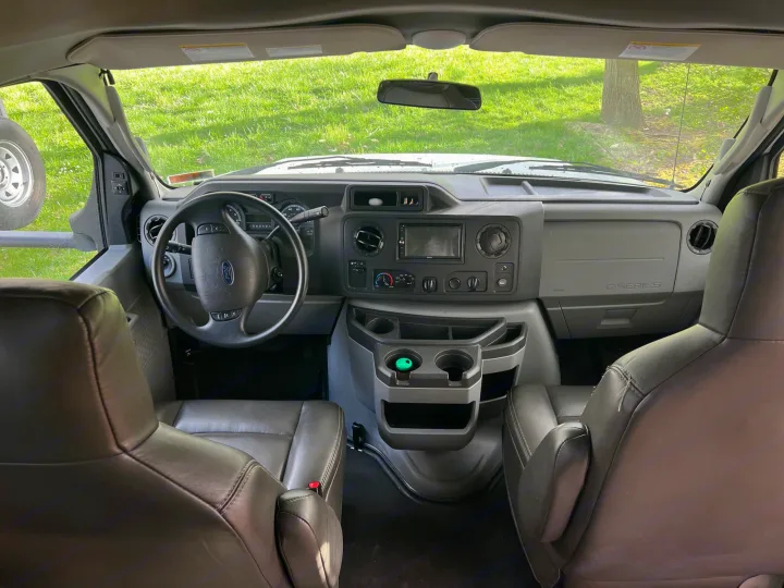 Spacious rv rental front cabin interior. Features dashboard, steering wheel, comfortable seats, and center console. Green grass outside.. Forest River Sunseeker Classic 2020