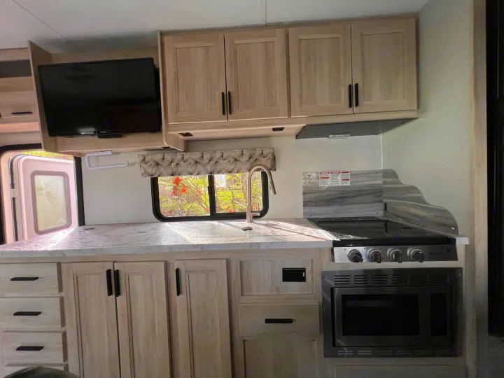 Well-equipped RV rental kitchen: light wood cabinets, sink, stove, microwave, and mounted TV. Ready for your next adventure.. Forest River Sunseeker Classic 2020