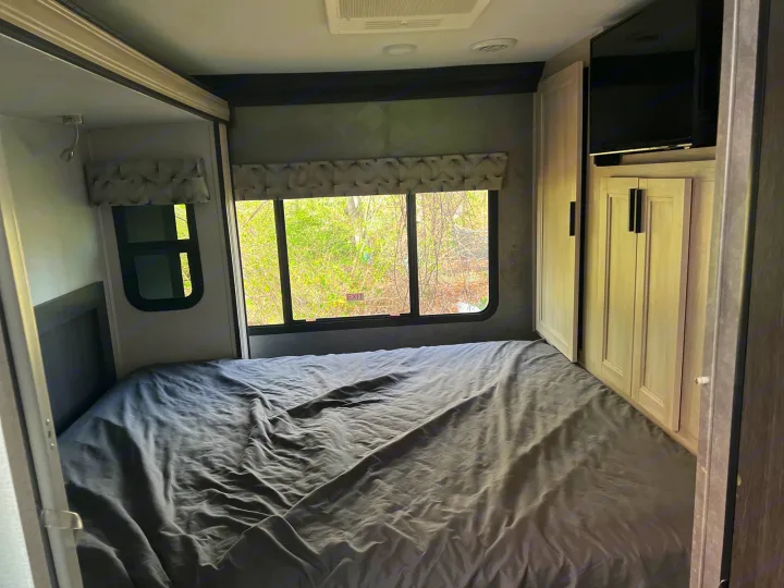 Explore this RV rental bedroom: cozy bed, large windows, storage cabinets, and a mounted TV for your travels.. Forest River Sunseeker Classic 2020