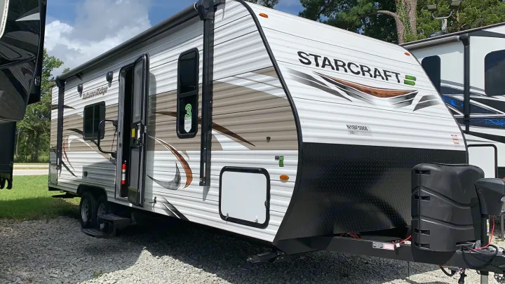 A white Starcraft Autumn Ridge travel trailer, featuring an open door, side awning, and front propane tanks, suitable for RV rental.. Starcraft Autumn Ridge 2022