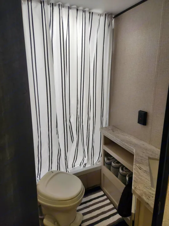 Compact rv rental bathroom with black/white striped shower curtain, toilet, vanity, & striped rug.. Starcraft Autumn Ridge 2022