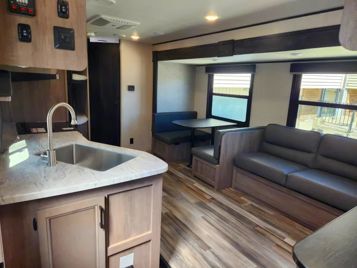 Modern RV rental interior features a well-appointed kitchen, cozy dining booth, and comfortable sofa seating on wood-look flooring.. Starcraft Autumn Ridge 2022