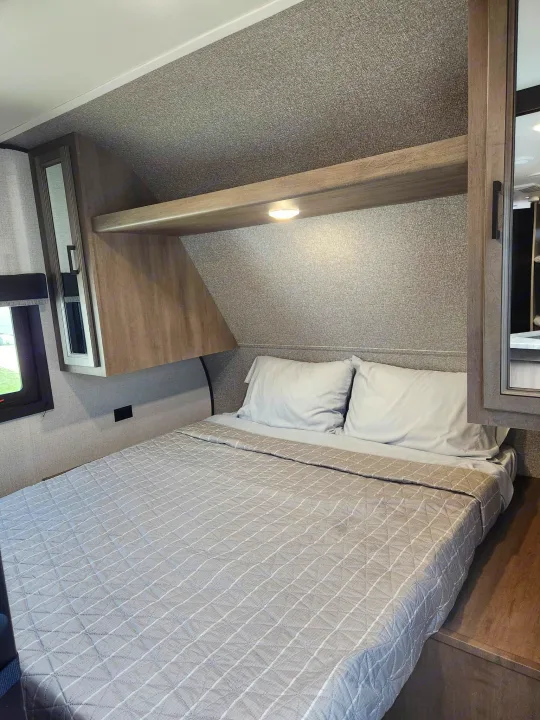 Relax in this modern RV rental bedroom, with a comfortable bed, overhead storage, and a window for natural light.. Starcraft Autumn Ridge 2022
