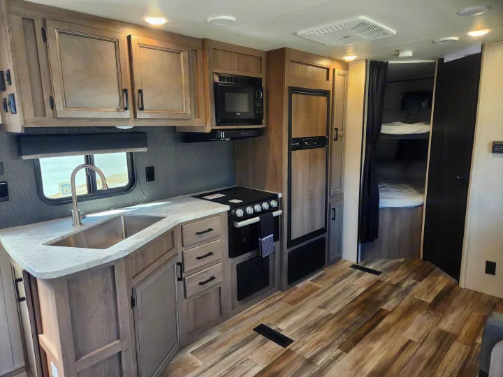 Spacious RV rental interior showing a modern kitchen with sink, microwave, stove, fridge, and a cozy bunk bed area.. Starcraft Autumn Ridge 2022