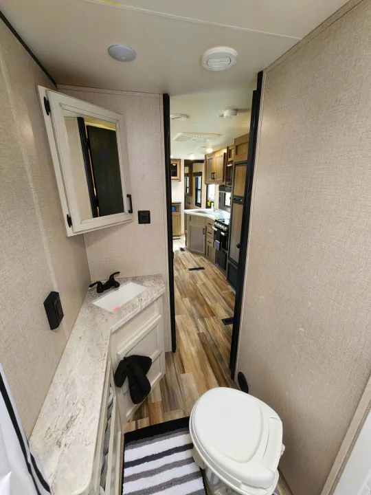 Explore this clean RV rental interior: a modern bathroom with toilet & vanity leads to a full kitchen and living area.. Starcraft Autumn Ridge 2022