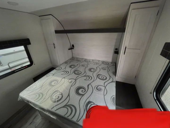 An RV rental bedroom features a bed with grey patterned mattress, built-in wardrobes, and windows on both sides.. K-Z Manufacturing Sportsman Classic 2022