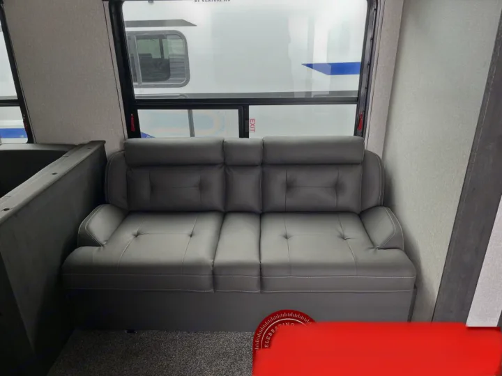 This RV rental's interior features a cozy gray sofa with tufted cushions, large windows, and a carpeted floor in a modern travel trailer.. K-Z Manufacturing Sportsman Classic 2022