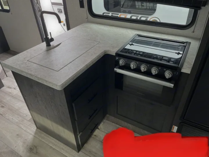 RV rental kitchen featuring a modern sink, sleek black stovetop with an oven, and dark wood-look cabinetry.. K-Z Manufacturing Sportsman Classic 2022