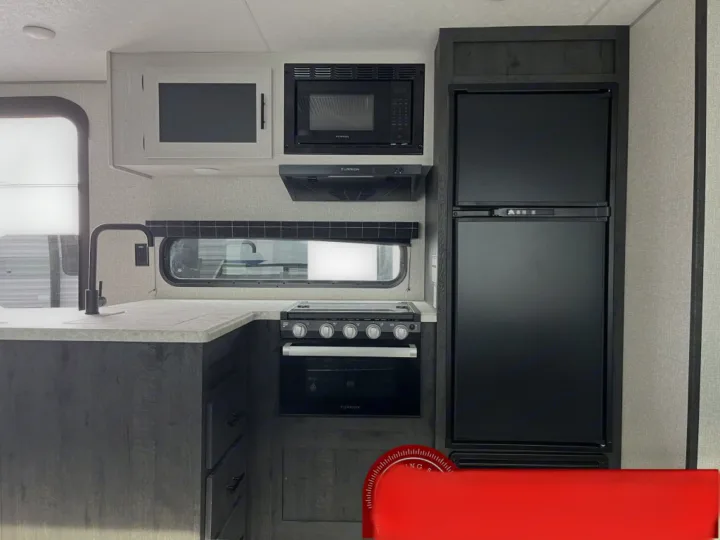 Modern RV rental kitchen with black appliances: microwave, range, large fridge, sink, and grey cabinetry.. K-Z Manufacturing Sportsman Classic 2022