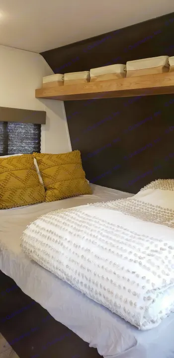 Modern RV rental bedroom: comfy bed with textured white bedding, yellow pillows, & storage shelf.. Keystone RV Springdale 2022