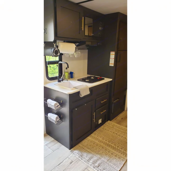 RV rental kitchen: modern dark cabinets, white counter, sink, stove, microwave, and practical storage solutions.. Keystone RV Springdale 2022