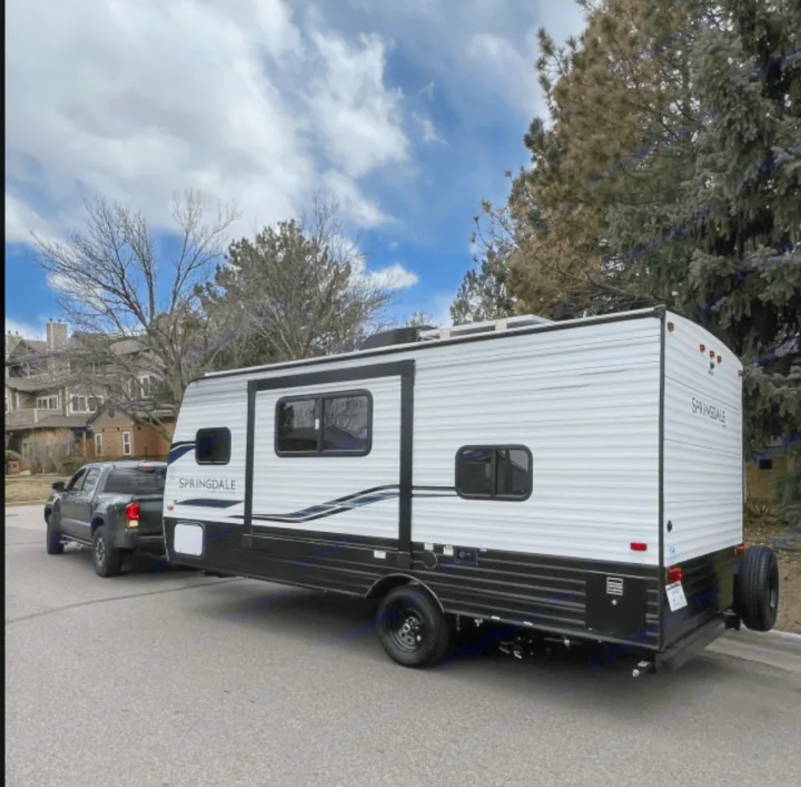 A white RV rental travel trailer, ready for adventure, hitched to a pickup truck on a street. Perfect for camping trips.. Keystone RV Springdale 2022