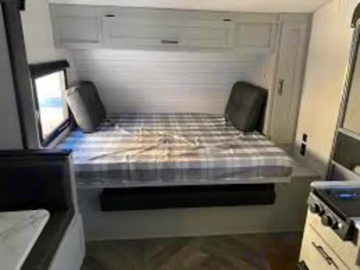 Cozy RV rental interior showing a built-in bed with plaid bedding, overhead cabinets, and a side window. Ideal for travel.. Forest River Salem FSX 178bhsk 2023