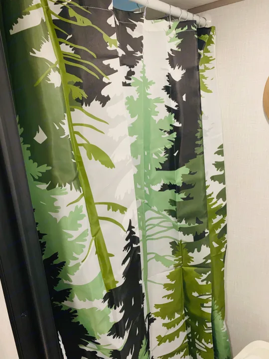 A green and black tree-patterned shower curtain, likely in an RV rental, hangs from a white rod with metal hooks.. Dutchmen Coleman Lantern LT 2023
