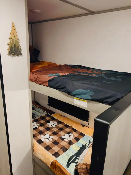 RV rental interior: Stacked bunk beds with unique nature and paw print bedding, ideal for family camping.. Dutchmen Coleman Lantern LT 2023