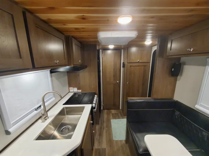 Cozy RV rental interior featuring a kitchen with sink, stovetop, wood cabinets, and a dining booth with table. Wooden ceiling.. Imperial Outdoors XploreRV 2023