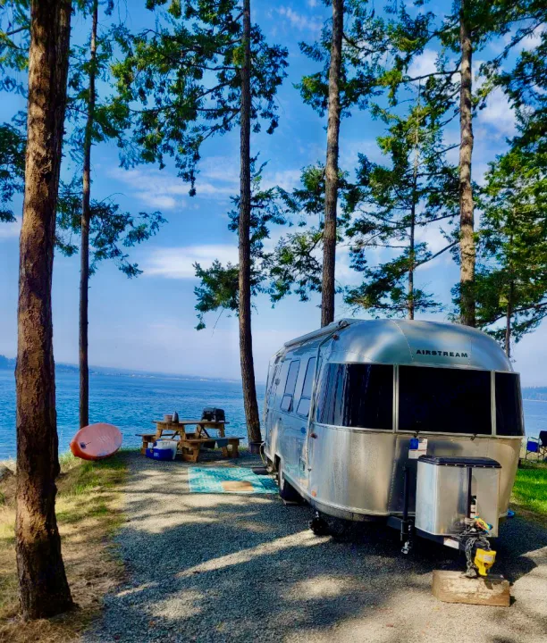 A sleek Airstream RV rental parked at a tranquil waterfront campsite, offering stunning views and a perfect nature escape.. Airstream Sport 2019
