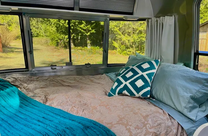 Relax in this RV rental bedroom: A comfortable bed with patterned bedding and blue pillows overlooks a serene natural view.. Airstream Sport 2019