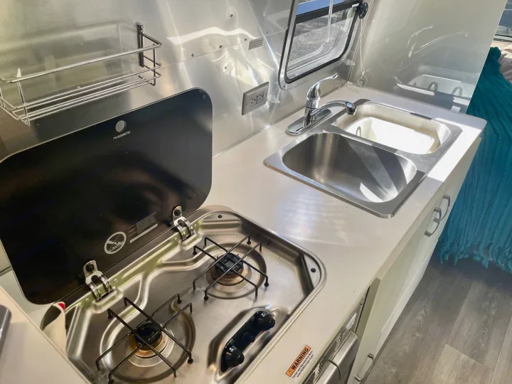 Modern RV rental kitchen with a Dometic gas cooktop, stainless steel sink, and wall outlet, ideal for your next trip.. Airstream Sport 2019