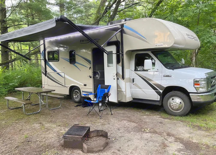 RV rental at a wooded campsite: a Thor Freedom Elite with awning extended, plus a picnic table and fire pit.. Thor Freedom Elite 2018