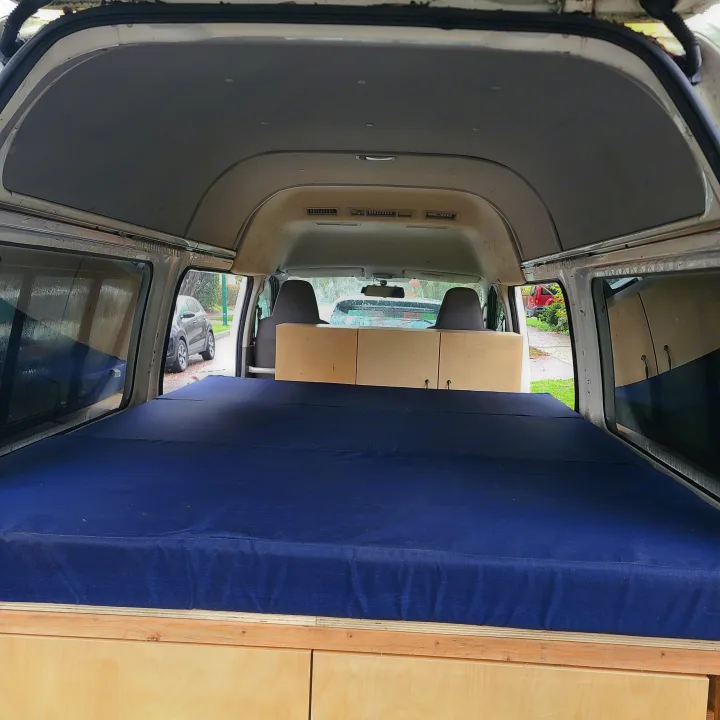 RV rental interior: A blue bed runs along the left, with light wood storage cabinets on the right. Functional camper van design.. Toyota Hiace 2006