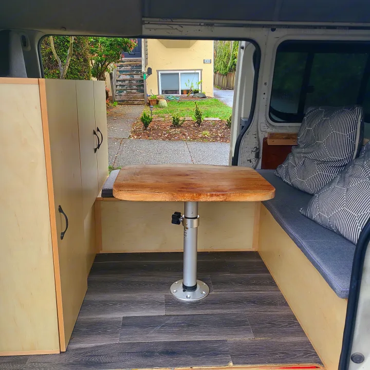 Custom RV rental interior featuring a clever adjustable wooden table, patterned pillows on seating, wood storage, and dark floor.. Toyota Hiace 2006