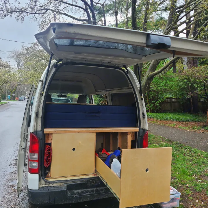 RV rental van's rear interior: custom bed and wooden storage setup, ideal for travel and mobile living.. Toyota Hiace 2006