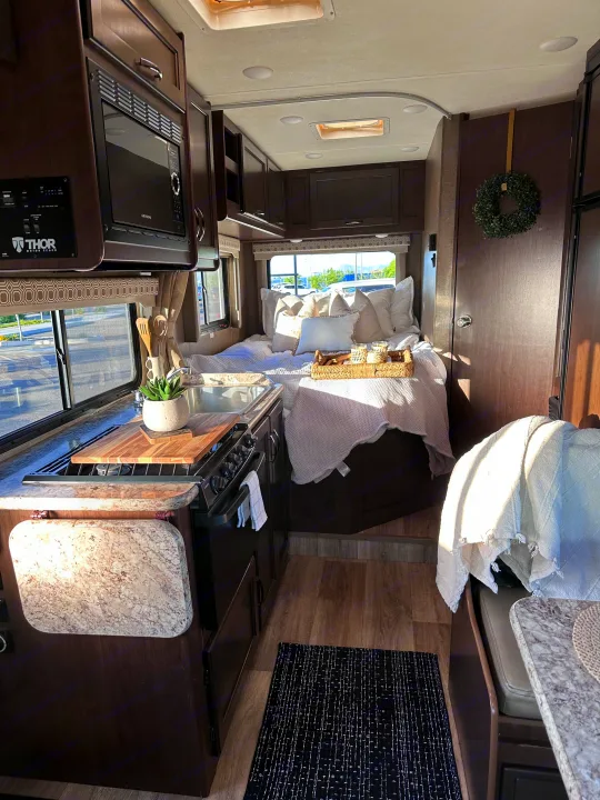 Experience cozy comfort in this stylish RV rental interior, featuring a compact kitchen, serene bedroom, and thoughtful decor.. Thor Four Winds 2020