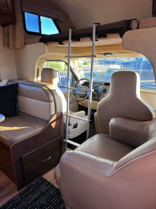 Inside a cozy RV rental: a ladder leads to the bunk bed, with dinette seating on the left and the driver's cabin ahead.. Thor Four Winds 2020