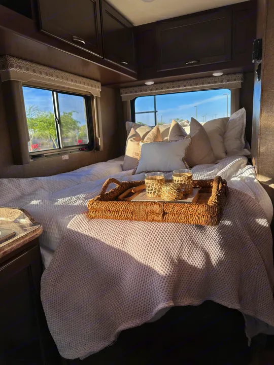Sunny RV rental interior: A cozy bedroom space with a neatly made bed, decorative pillows, and a wicker tray with glasses.. Thor Four Winds 2020