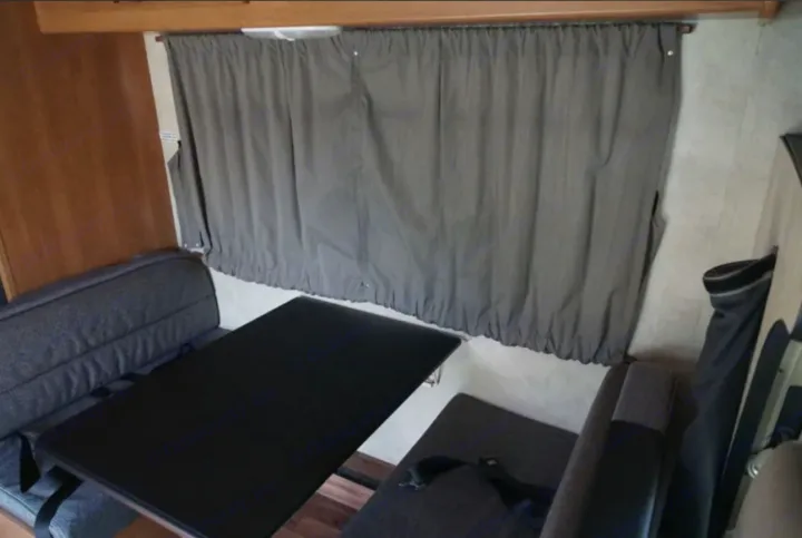 Inside this RV rental: a practical dinette with a black table, grey bench seating, and window curtains. Ideal for mobile living.. Thor Majestic 2012
