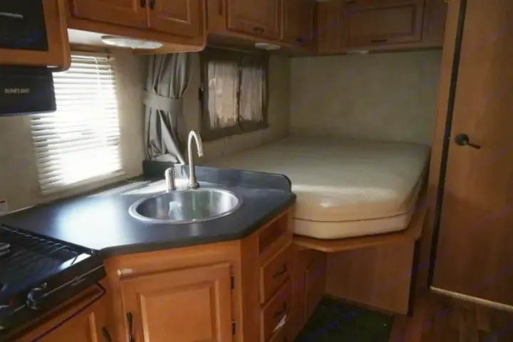 RV rental interior showing a compact kitchen with sink and stovetop, leading to a cozy bedroom area.. Thor Majestic 2012