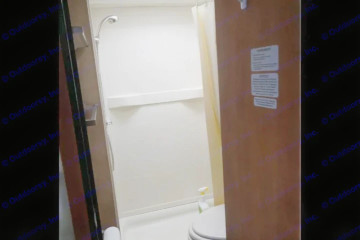 Inside an RV rental: a compact bathroom featuring a shower with curtain, part of a toilet, and cleaning items.. Thor Majestic 2012