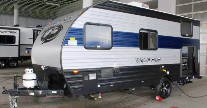 A gray and blue Wolf Pup travel trailer, a compact and modern rv rental, is parked indoors with its rear door open.. Forest River Cherokee Wolf Pup 2022