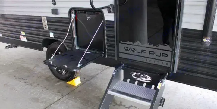 Side of a modern RV rental, a Wolf Pup travel trailer, showing its exterior utility door with a fold-down table and entry steps.. Forest River Cherokee Wolf Pup 2022