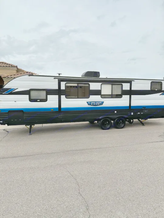 This modern white, black, and blue travel trailer, an RV rental, is parked on asphalt under a cloudy sky, ready for your next adventure.. Forest River Salem Cruise Lite T282QXBL 2023