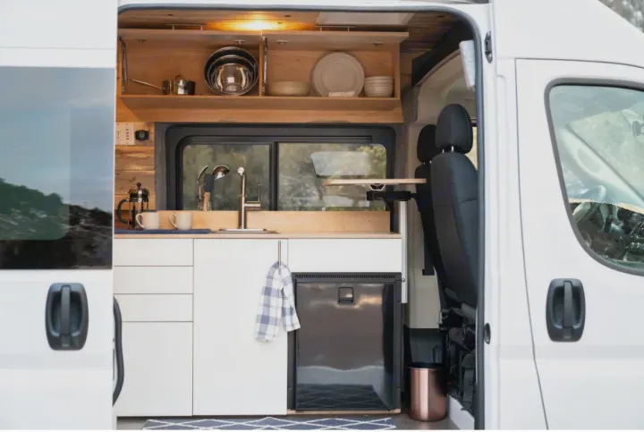 RV rental: Bright, modern camper van kitchen with sink, under-counter fridge, and wood cabinets, ready for travel.. Dodge Sprinter Van 2020