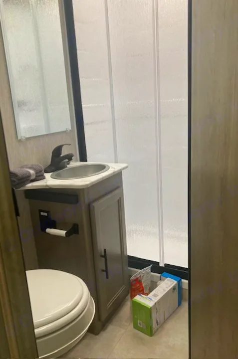 Inside an RV rental, a small bathroom features a toilet, vanity with sink, mirror, and shower stall.. Coachmen 26DS 2021