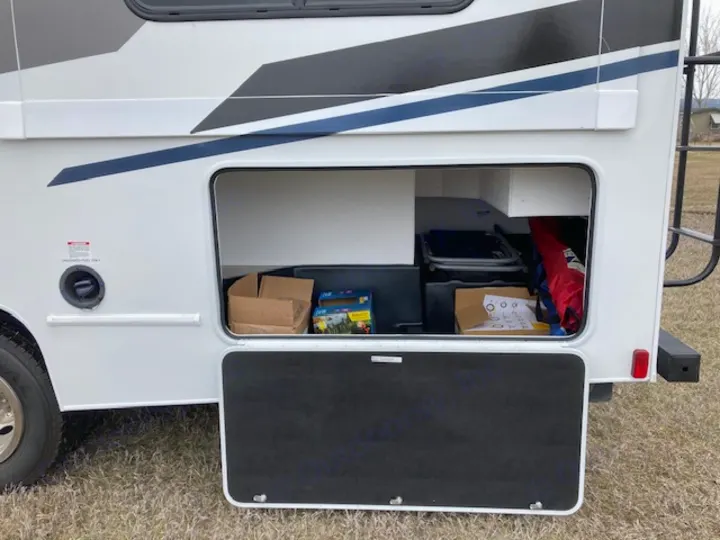 This RV rental shows its spacious exterior storage bay open, filled with boxes, a folded chair, and other travel gear.. Coachmen 26DS 2021