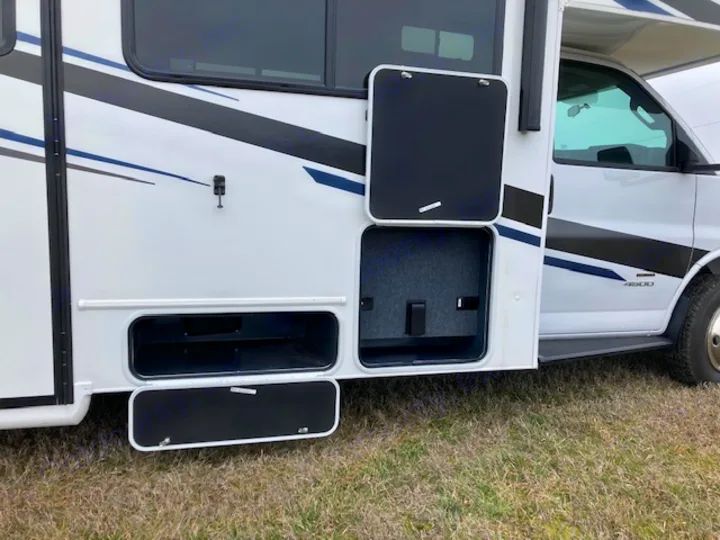 Side view of a white RV rental. Open exterior storage compartments reveal spacious, accessible storage for your travel needs.. Coachmen 26DS 2021